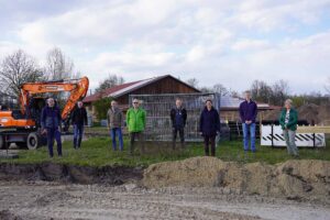 Mitglieder der SPD-Dollbergen stehen aufgereiht vor der Baustelle des Parkplatzes, im Hintergrund ein Bagger und die Mix-Firmenhalle.